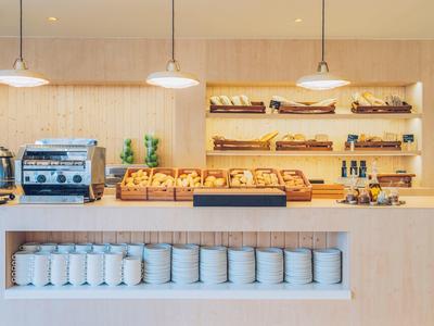 Moderne Bäckerei mit Holzregalen, Broten, Kaffeemaschine und weißen Vorratsbehältern unten.