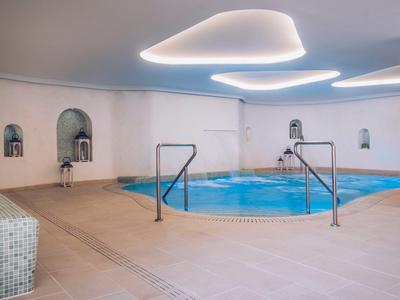 Innen-Schwimmbad mit runden Pool, Edelstahl-Geländern, beige Fliesen und modernen Deckenleuchten.