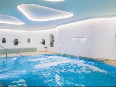 Ein moderner Hallenpool mit Wasserfall, glatten weißen Wänden und geschwungenen Deckenleuchten.