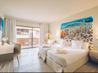 Helles Hotelzimmer mit zwei Betten, Schreibtisch, Fernseher und großem Aquarienbild an der Wand.