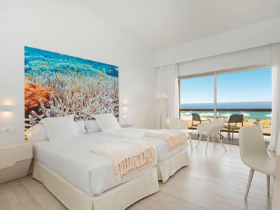 Helles Schlafzimmer mit zwei Betten, Meerblick, hellem Holzboden und großem farbigem Korallenbild.