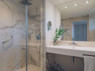 Modernes Bad mit großen Marmorfliesen, großer Spiegel, Dusche und einem Blumenarrangement.