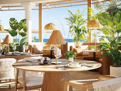 Ristorante luminoso con mobili in legno, piante verdi e vista mare alla luce del giorno.