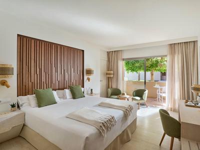 Camera d'hotel luminosa con due letti, accenti verdi e accesso a una terrazza con vista sul giardino