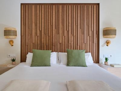 Camera d'hotel moderna con letto matrimoniale, cuscini verdi e testiera in legno.