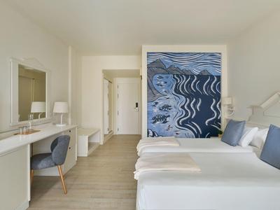 Camera d'hotel luminosa con due letti, grande opera d'arte astratta e area scrivania moderna.