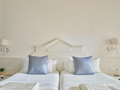 Due letti singoli bianchi con cuscini blu e comodini in una luminosa camera d'hotel.