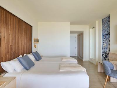 Camera d'hotel con due letti matrimoniali, parete in legno, sedie e design minimalista.