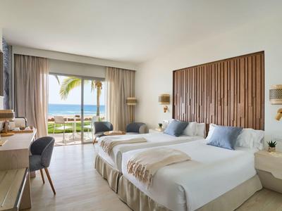 Camera d'hotel moderna con due letti, scrivania, TV e vista mare attraverso grandi finestre