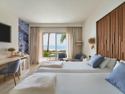 Camera d'hotel moderna con due letti, vista mare e arredi accoglienti.