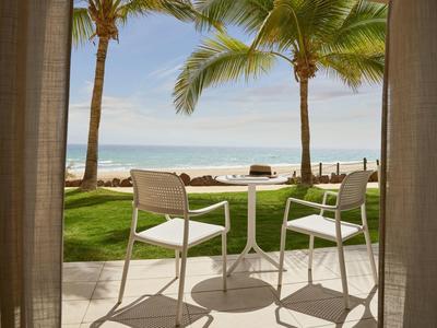 Due sedie e un tavolo rotondo su una terrazza con vista su palme, prato e mare