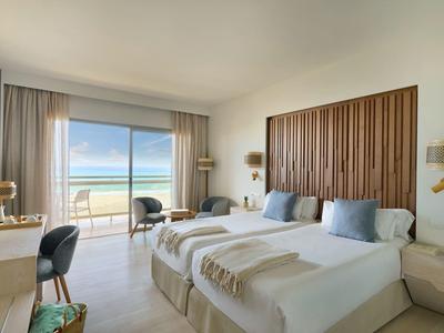 Camera d'hotel moderna con due letti e vista mare attraverso grandi porte scorrevoli in vetro.