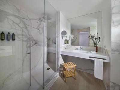 Bagno moderno con pareti in marmo, doccia in vetro, grande specchio e sgabello in legno