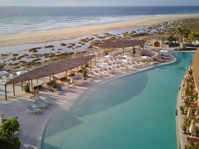 Grande piscina con lettini che si affaccia su una spiaggia sabbiosa e sul mare in una giornata di sole