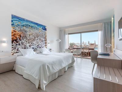 Helles Schlafzimmer mit Doppelbett, großem Meeresbild, Schreibtisch, und Balkon mit Meerblick.