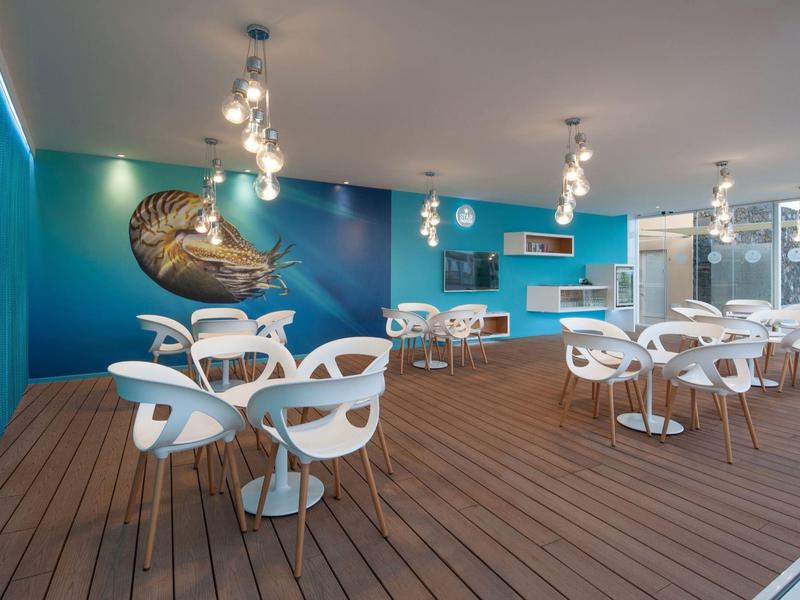 Sala da pranzo moderna e colorata con sedie bianche e pavimento in legno, illuminata da luci a soffitto.