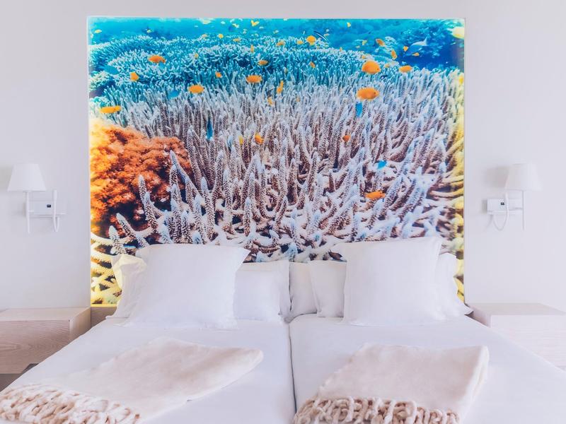 Letto matrimoniale moderno con biancheria bianca davanti a una parete con grande foto di barriera corallina