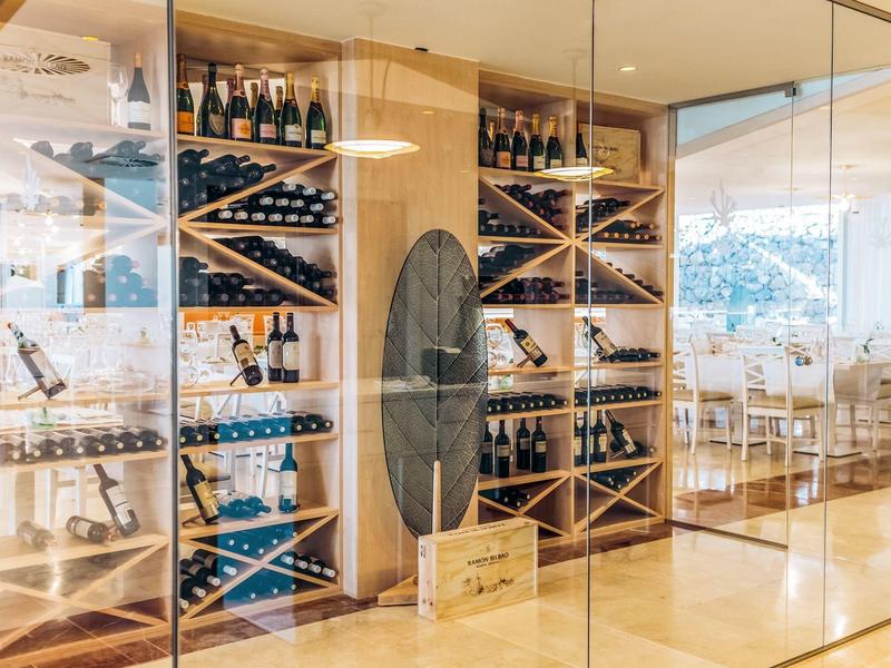 Cantina vini con scaffali in legno e varie bottiglie di vino in una stanza moderna con pareti di vetro.