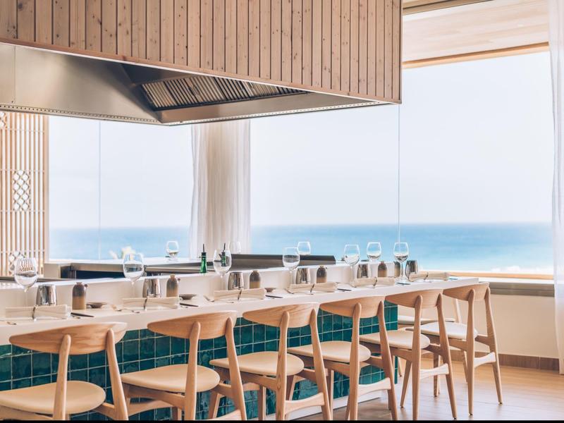 Sala da pranzo luminosa con mobili in legno e vista sul mare attraverso grandi finestre