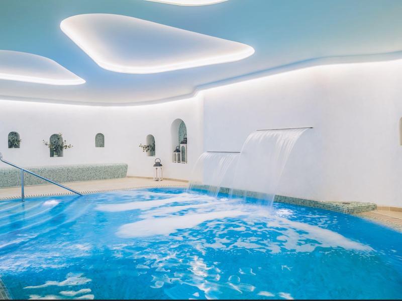 Piscina interna moderna con pareti bianche curve e cascata.