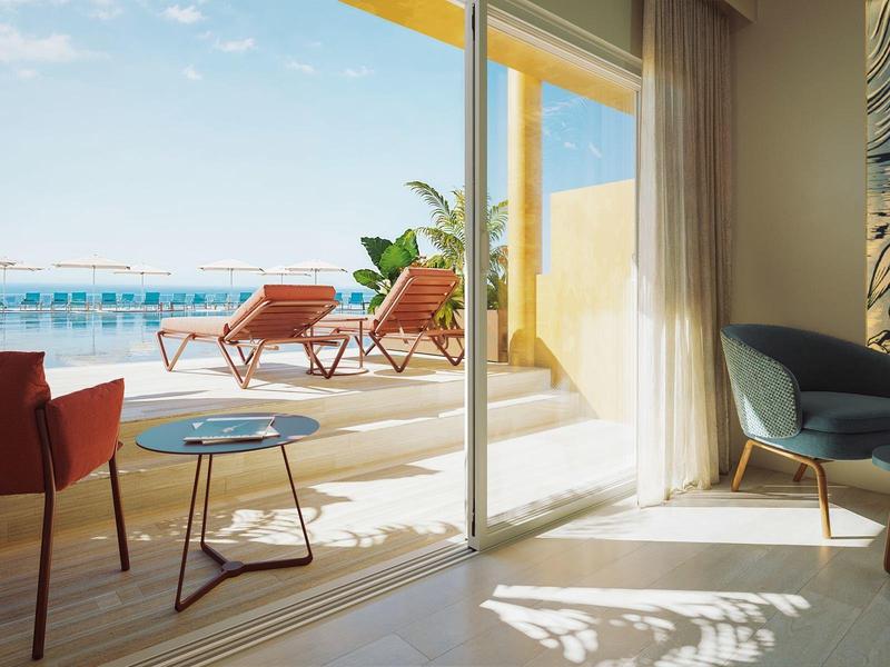 Camera d'hotel luminosa con terrazza, sedie e vista su una piscina con tempo soleggiato.
