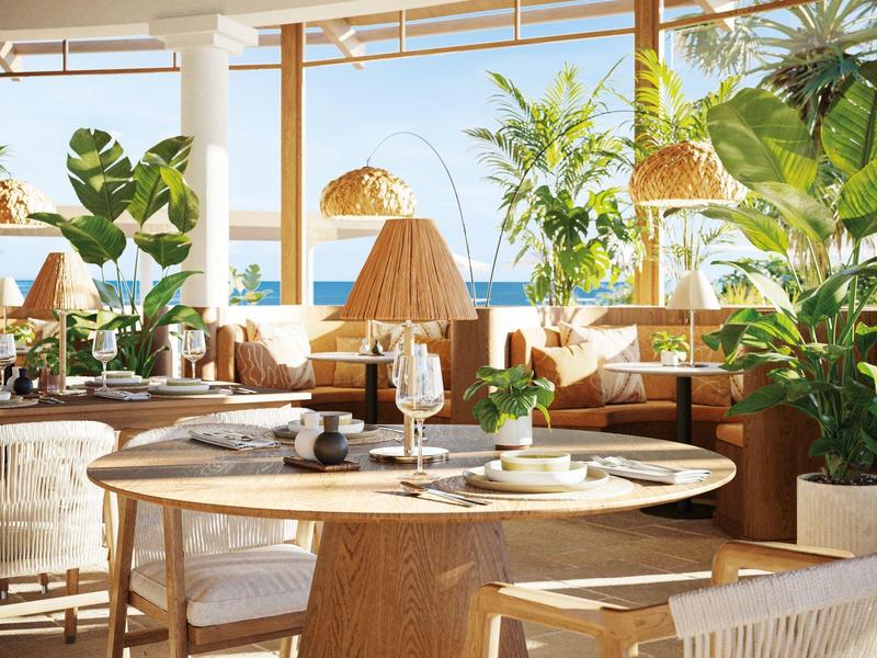 Zona pranzo luminosa con legno e piante, grandi finestre e vista sul mare.