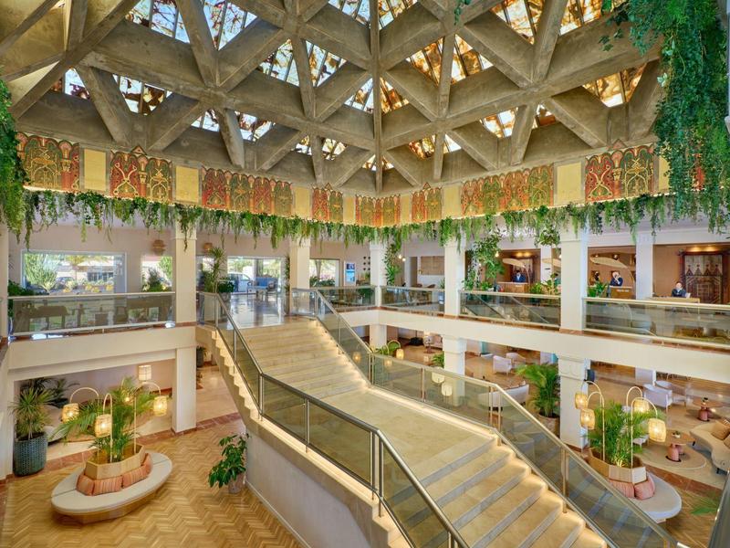 Interno di hotel luminoso con scale, piante e soffitto decorativo