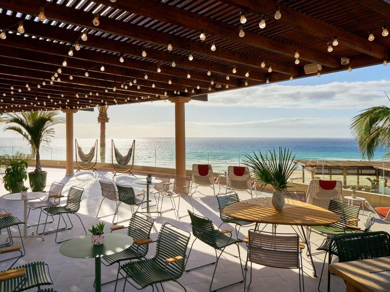 Terrazza aperta con tavoli, sedie e vista mare sotto un tetto in legno con luci a filo