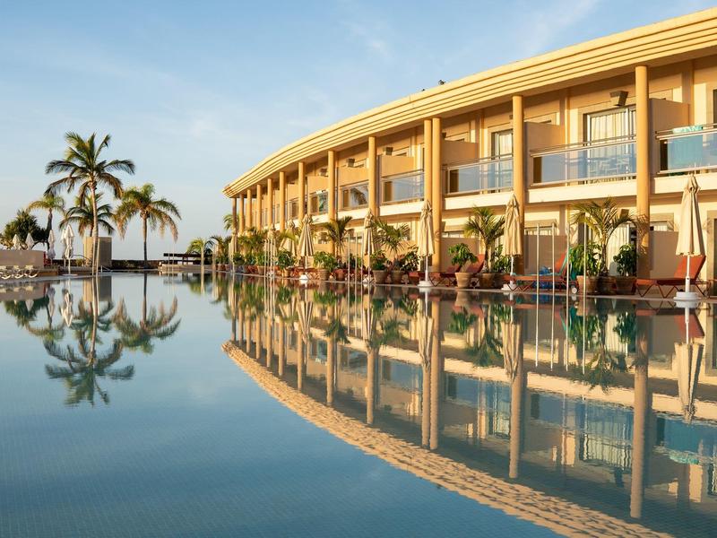 Edificio dell'hotel moderno con piscina lunga e palme al tramonto.