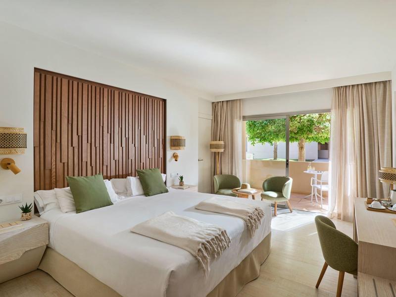 Camera d'hotel luminosa con due letti, accenti verdi e accesso a una terrazza con vista sul giardino