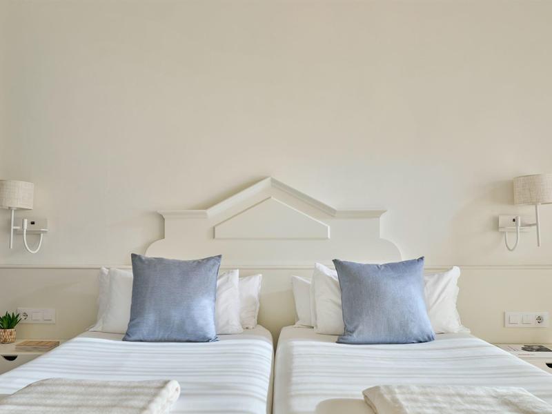 Due letti singoli bianchi con cuscini blu e comodini in una luminosa camera d'hotel.