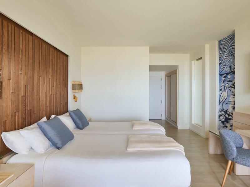 Camera d'hotel con due letti matrimoniali, parete in legno, sedie e design minimalista.