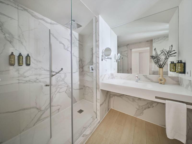 Bagno moderno con doccia in vetro, grande specchio e pavimento in marmo chiaro.