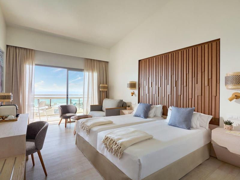 Camera d'hotel moderna con letto matrimoniale, balcone e vista mare.