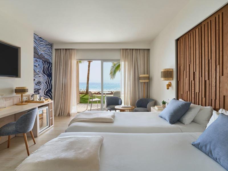 Camera d'hotel moderna con due letti, vista mare e arredi accoglienti.