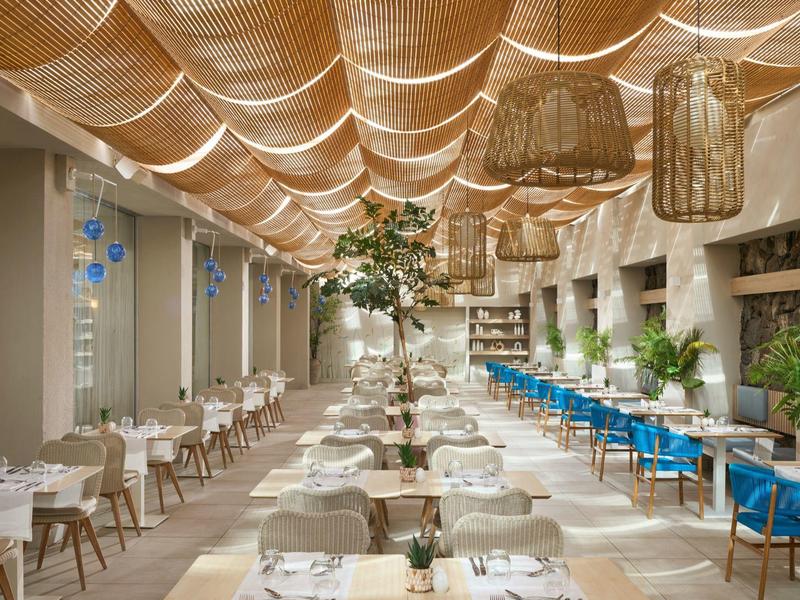 Ristorante moderno con tavoli bianchi, sedie blu e illuminazione elegante al soffitto