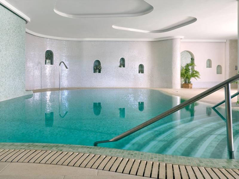 Piscina interna con acqua turchese, mosaico di piastrelle bianche e corrimano nell'area benessere.