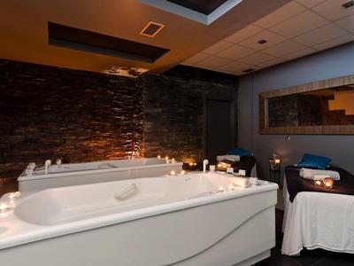 Salle de spa avec grande baignoire, fauteuils massants et ambiance lumineuse tamisée.