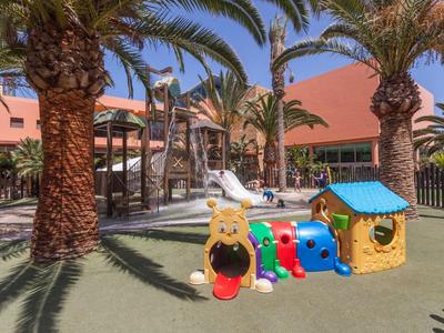 Aire de jeux pour enfants avec toboggans et structures colorées sous des palmiers.