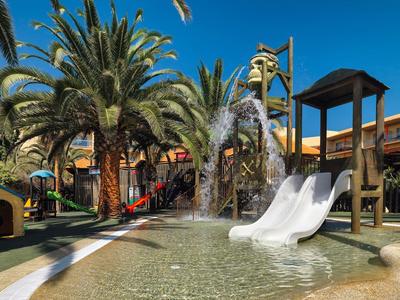 Aire de jeux avec toboggan et fontaine dans un jardin tropical d'hôtel.