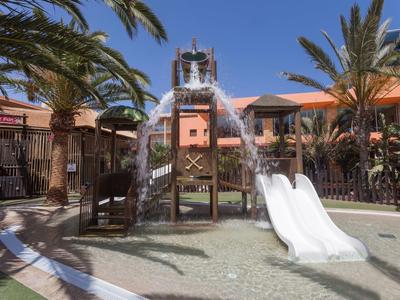 Aire de jeux avec toboggans blancs entourée de palmiers sous un ciel bleu.
