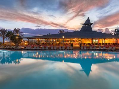 Luxuriöses Hotelrestaurant mit beleuchtetem Pool und Palmen bei Sonnenuntergang