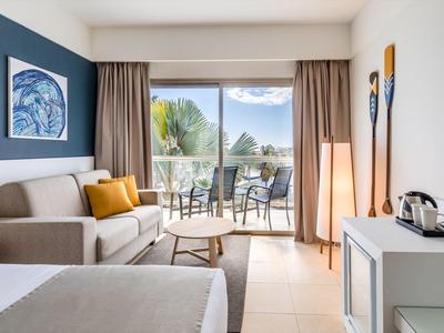 Chambre d'hôtel moderne avec canapé, table basse et balcon avec vue sur la nature.