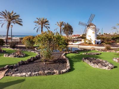 Grüner Minigolfplatz mit Windmühle und Palmen unter blauem Himmel