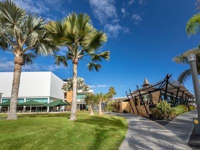 Moderner Außenbereich mit Palmen, Rasen und Gebäuden unter blauem Himmel.