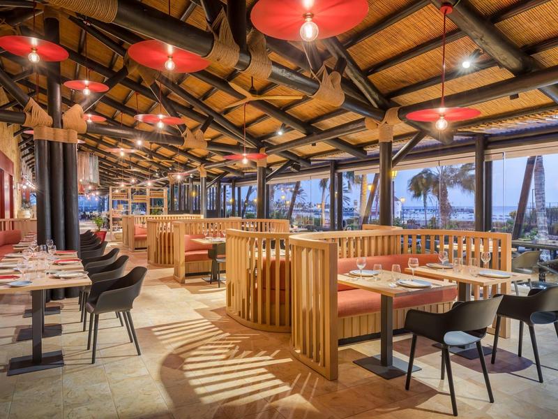 Restaurant en terrasse avec ambiance chaleureuse et vue sur la mer au coucher du soleil.