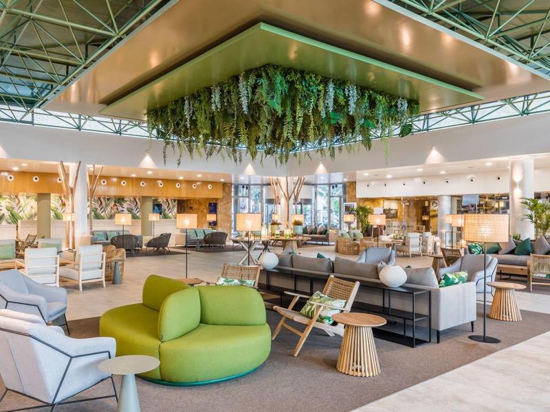 Salon d'hôtel moderne avec sièges verts et blancs, décoration suspendue et lumière naturelle.