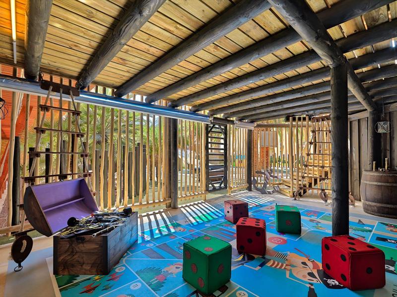 Salle de jeux avec dés géants colorés sur un sol moquetté sous un plafond en bois.