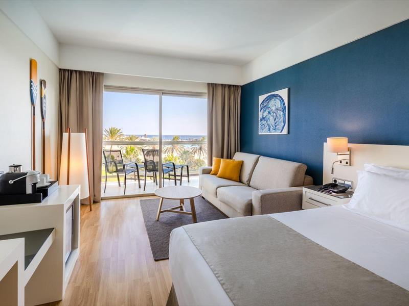 Chambre d'hôtel moderne avec un grand lit, un canapé, un balcon et vue extérieure.