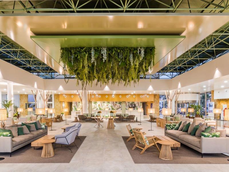 Grand hall lumineux avec canapés, tables en bois et plantes suspendues au plafond.